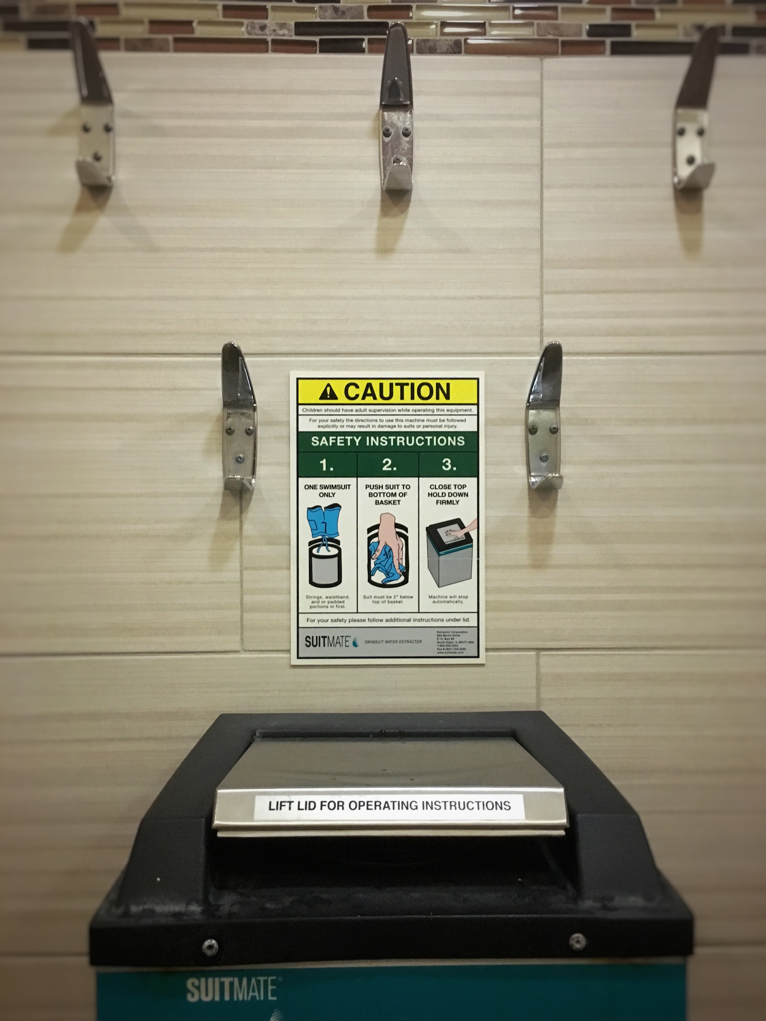 A swimsuit dryer -which is a box on a wall with a metal lid and a poster that has instructions for using it.