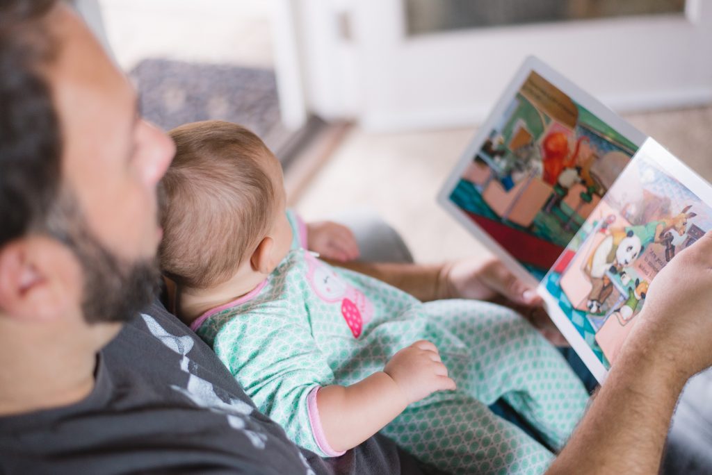 man holding a young infant on his lap reading a book