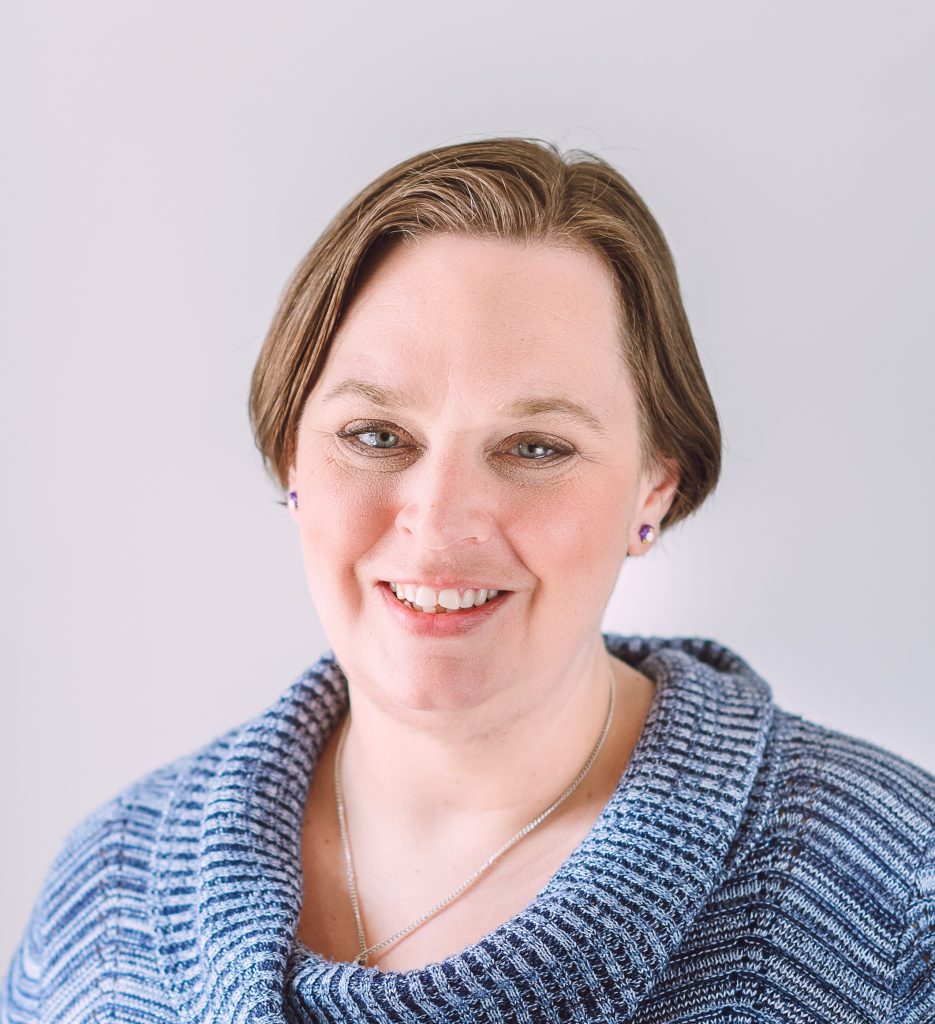 Jenn, a white woman with short light brown hair and blue eyes smiles at the camera.