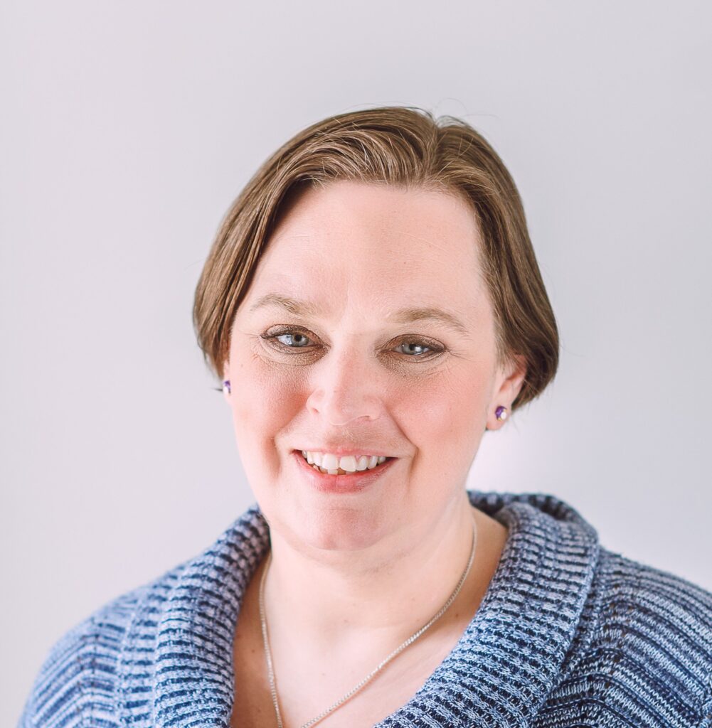 Jenn, a white woman with short light brown hair and blue eyes smiles at the camera.