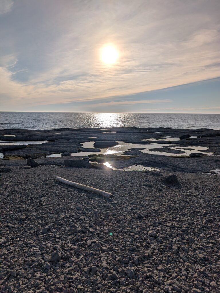 The sun sets over a tide pool with the ocean in the background